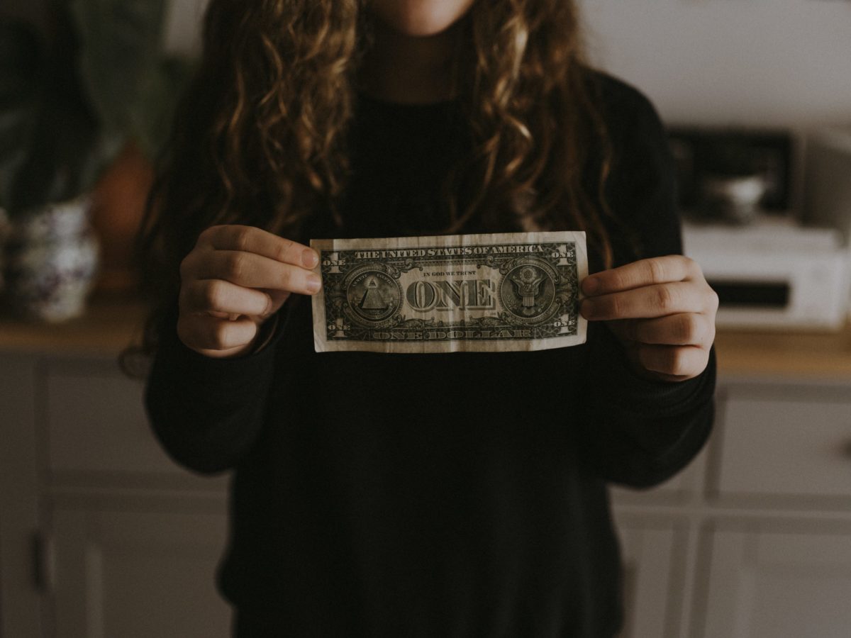 Photo of a person holding a U.S. dollar bill with its reverse side to the camera.