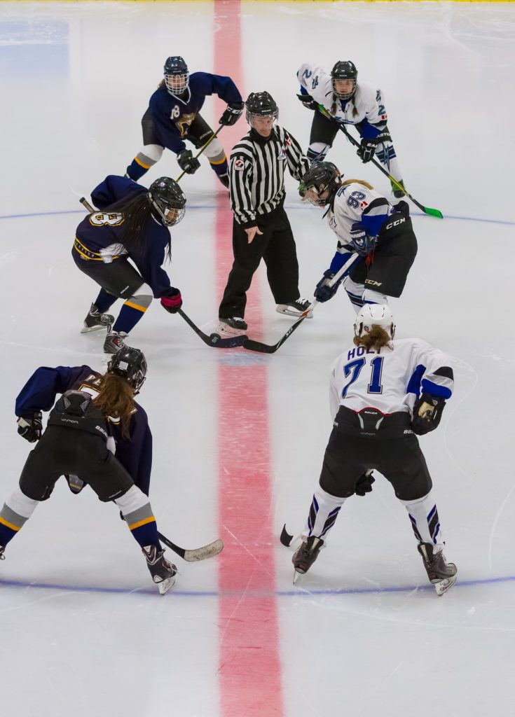 Two women's' ice hockey teams line up at the faceoff circle