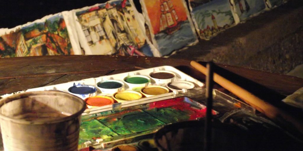 A palette of watercolors on the table and paintings drying in the background