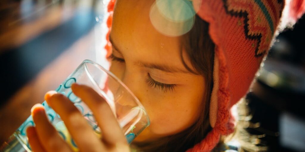 A young girl drinking water from a glass.