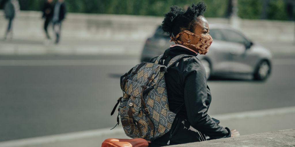 A photo of a woman in a face mask walking her bike on the street.